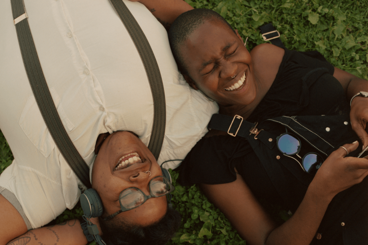 2 queer people laying on the grass laughing, representing the extra mental energy available once body image thoughts are peaceful. Body image therapy in California is available. 90401 | 90266 | 90094