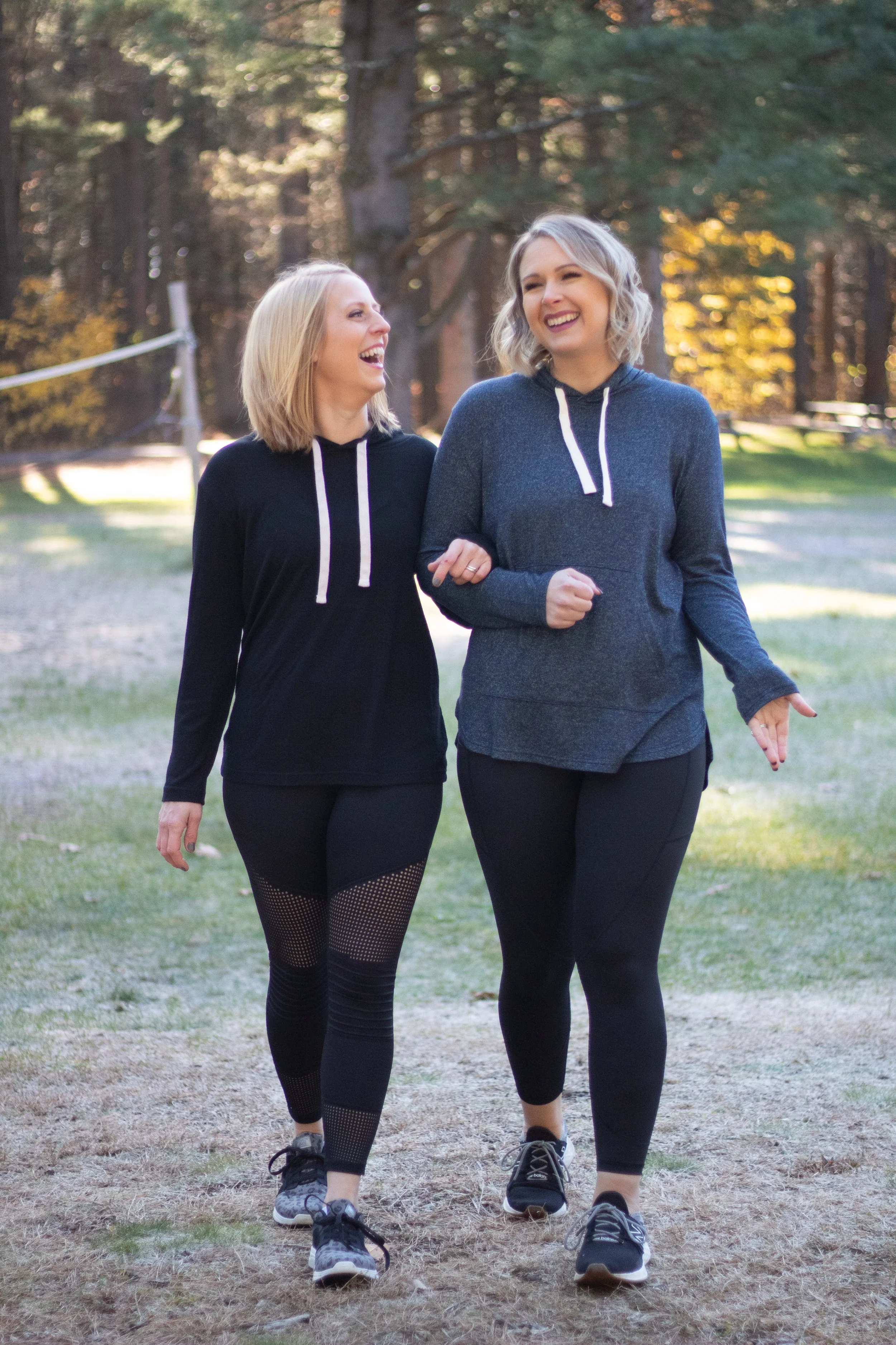 Two women friends walking through a park in the fall, laughing