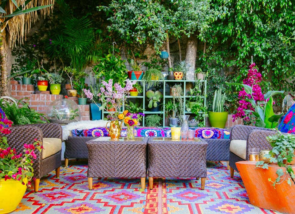 Colorful outdoor garden seating area with wicker chairs and couches, vibrant plants, and decorative items.