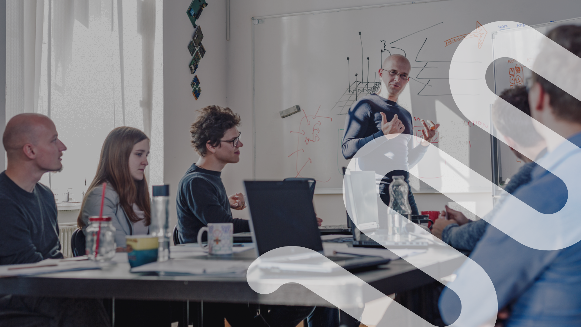 A business meeting with a graphic timeline on a computer screen showing the process of a request, bids, selection, compliance, time and expense, invoicing, and off boarding. There are two people working at the table with documents, a calculator, a tablet showing stock data, a notebook, and a glass of water.