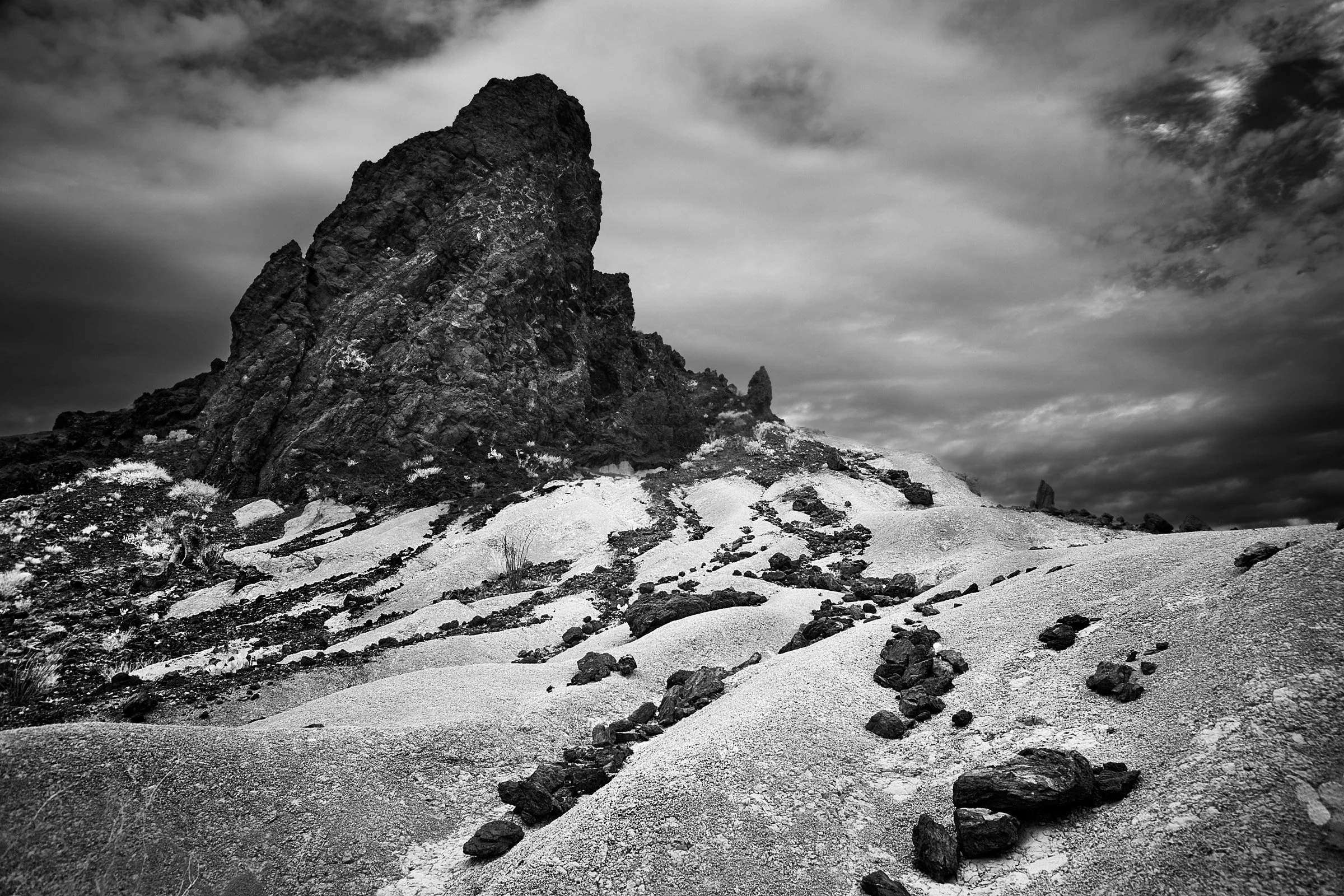 Spire Over Tuff Waves - A pale tuff slope forms ridges and shallow cuts, carrying scattered rock like ballast as the spire rises dark and steady behind it at Big Bend.
