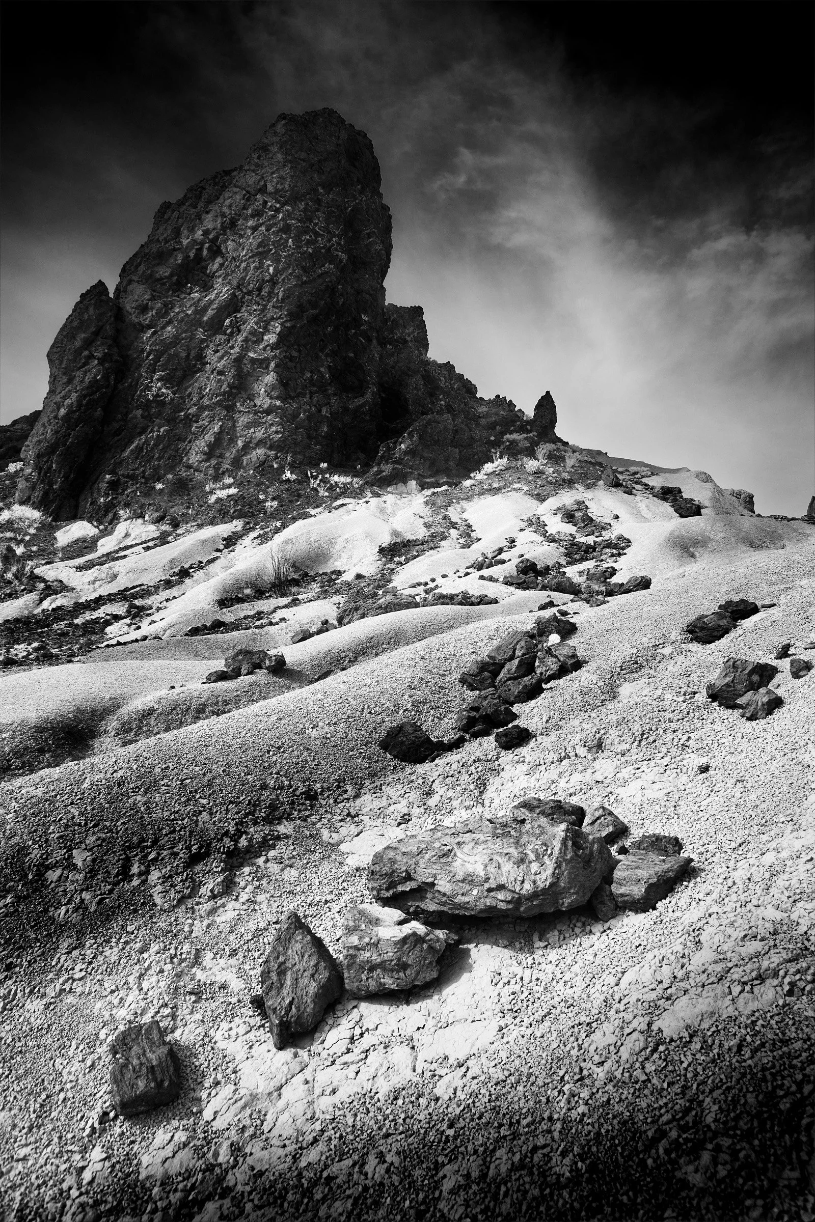 Tuff Dunes Under the Spire - A slope of tuff forms soft waves and scallops, holding scattered rock like ballast; above it, the spire keeps its sharp outline in Big Bend weather.