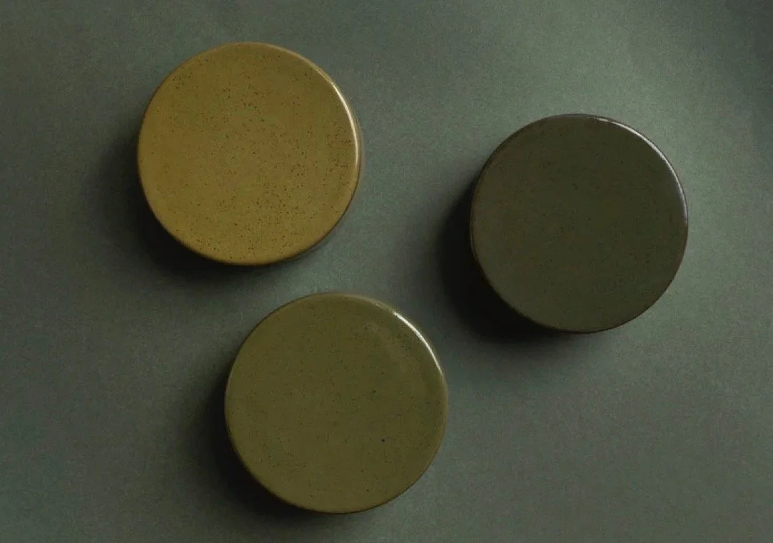 Three small, round, ceramic or wooden containers in yellow and green shades, placed on a flat surface