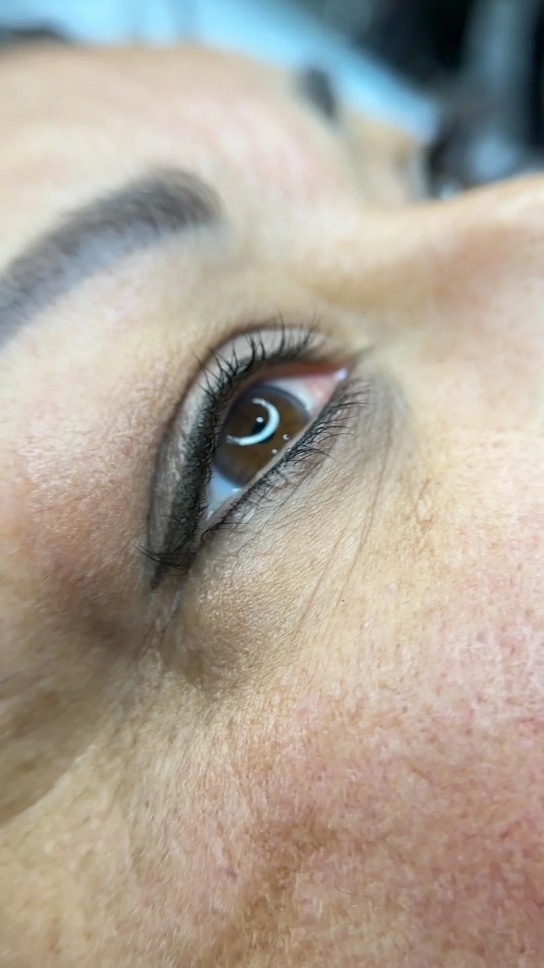 Close-up of a person's eye looking upward, with visible brown iris, eyelashes, eyebrow, and skin details.