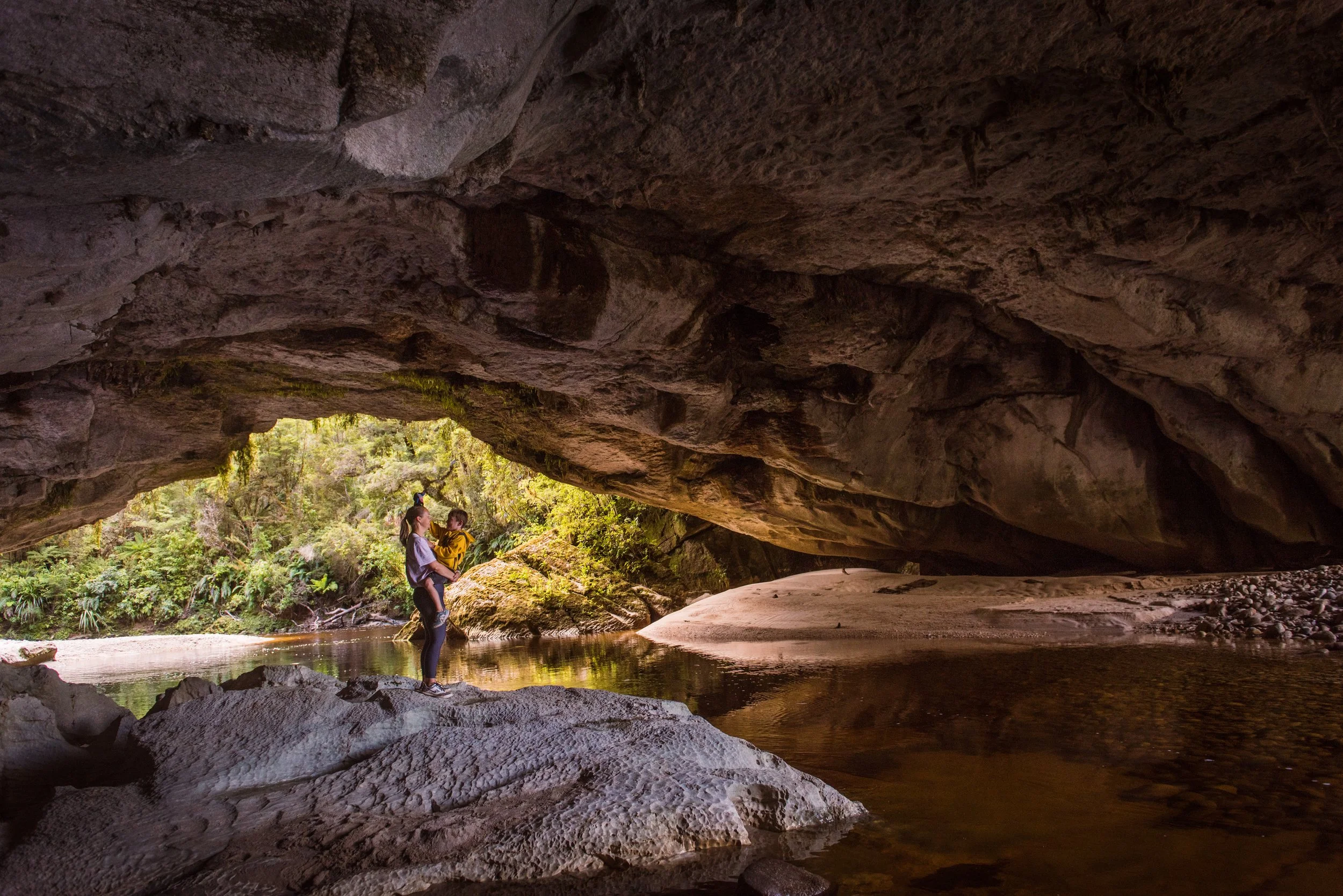 Mum and son standing in a cave by a river