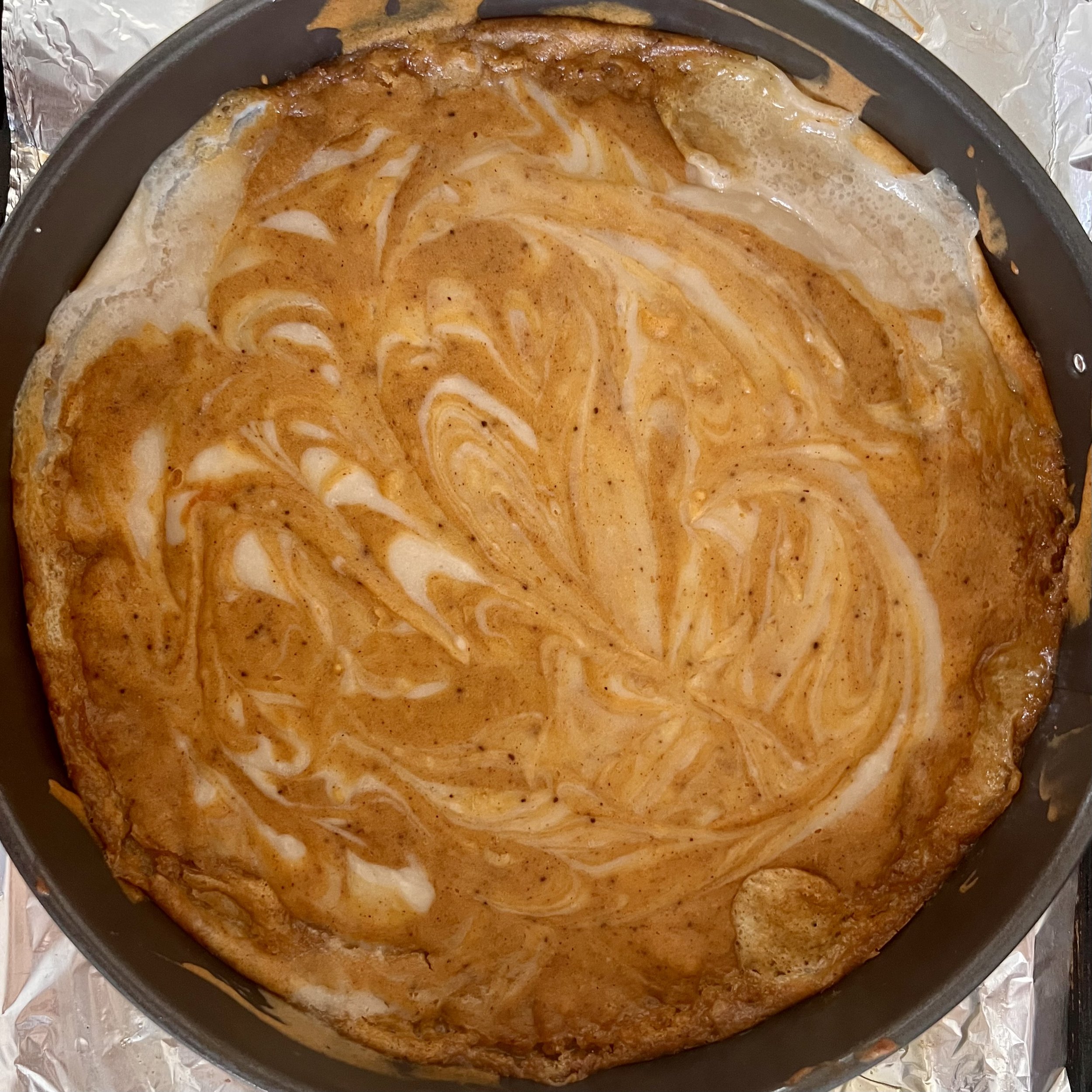 Marbled dairy free pumpkin cheesecake with swirls of caramel and vanilla in a round baking dish.
