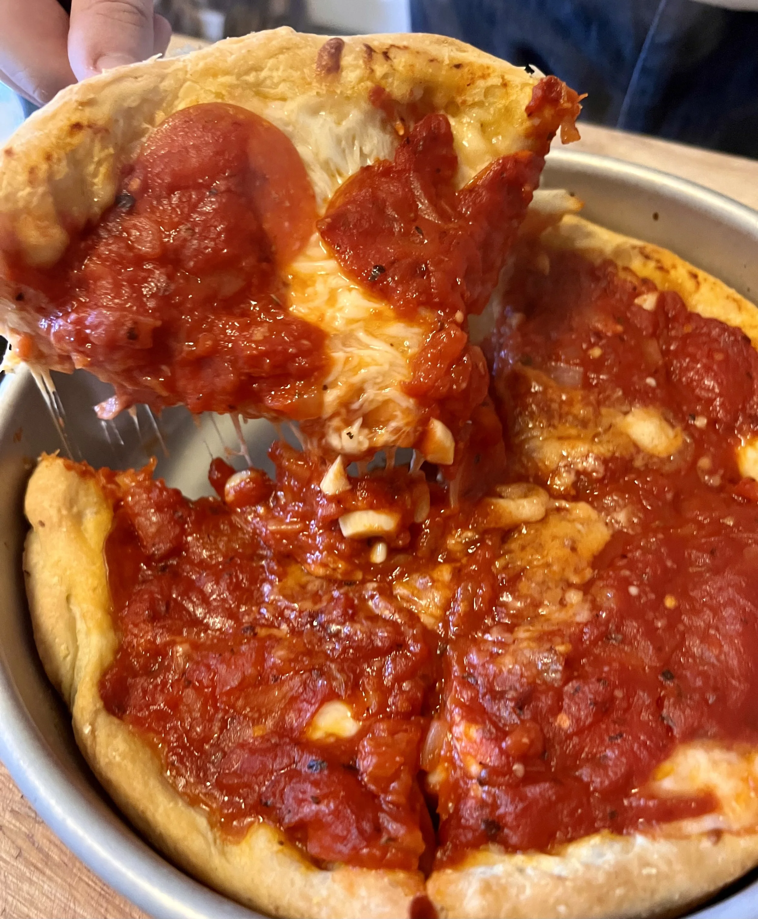 Close-up of a pepperoni and cheese pizza with a slice being lifted from the pan.