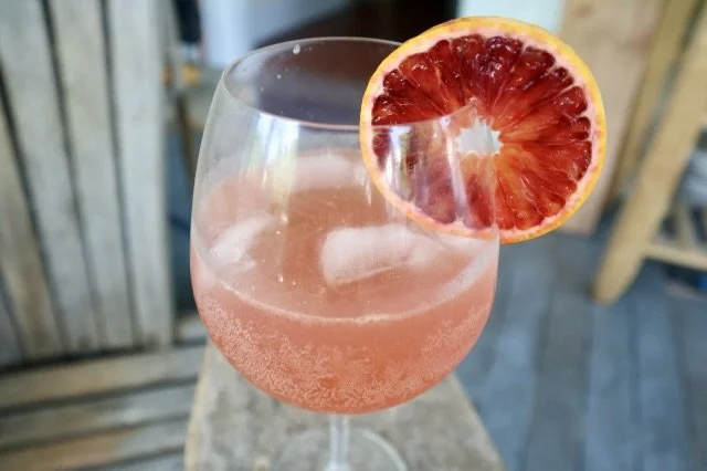 Sunset Spritz in a wine glass with a blood orange garnish