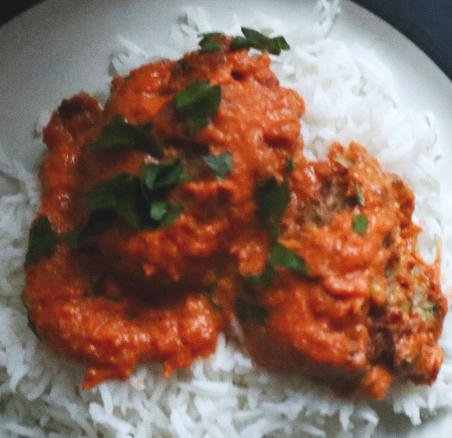 Close-up of a piece of dudhi kofta garnished with green herbs, served on a bed of white rice.