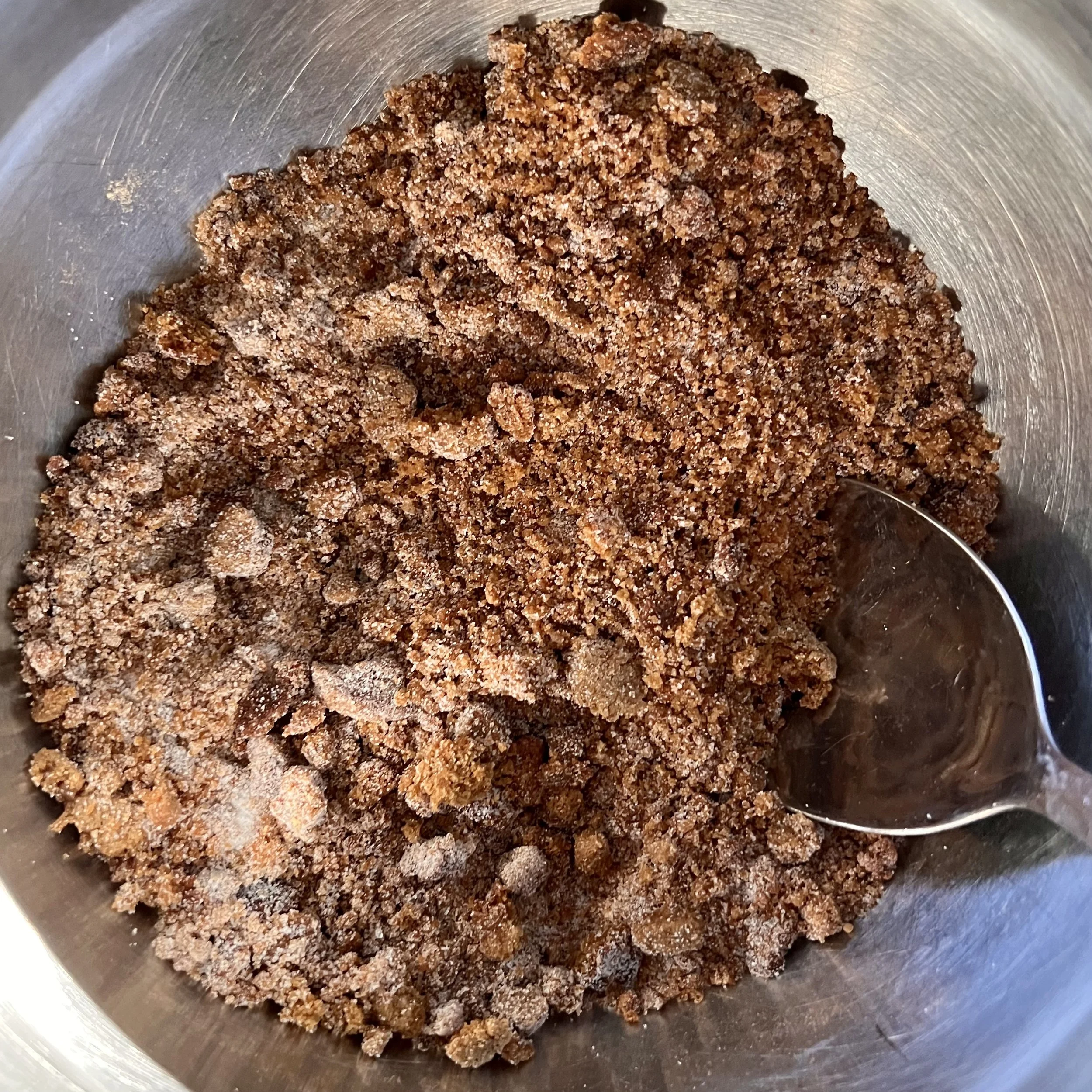 Close-up of a mixture of ground ginger snaps in a metal bowl with a spoon.