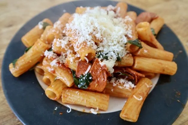 Pasta with a red sauce, plant-based pepperoni, basil, and Parmesan cheese