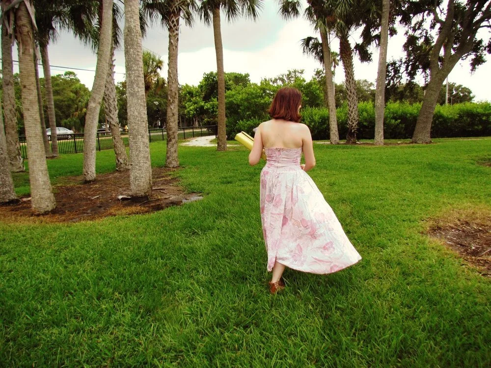 A girl in long, pink dress running in dark green grass in Florida