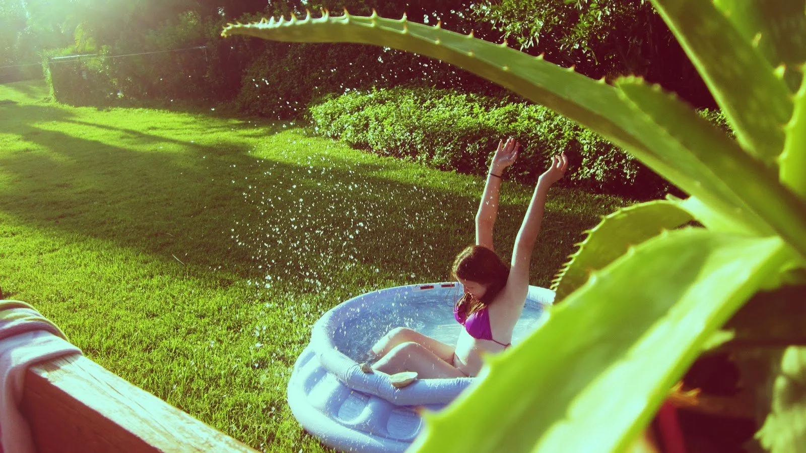 A young girl in a kiddie pool and a beautiful Green aloe vera plant