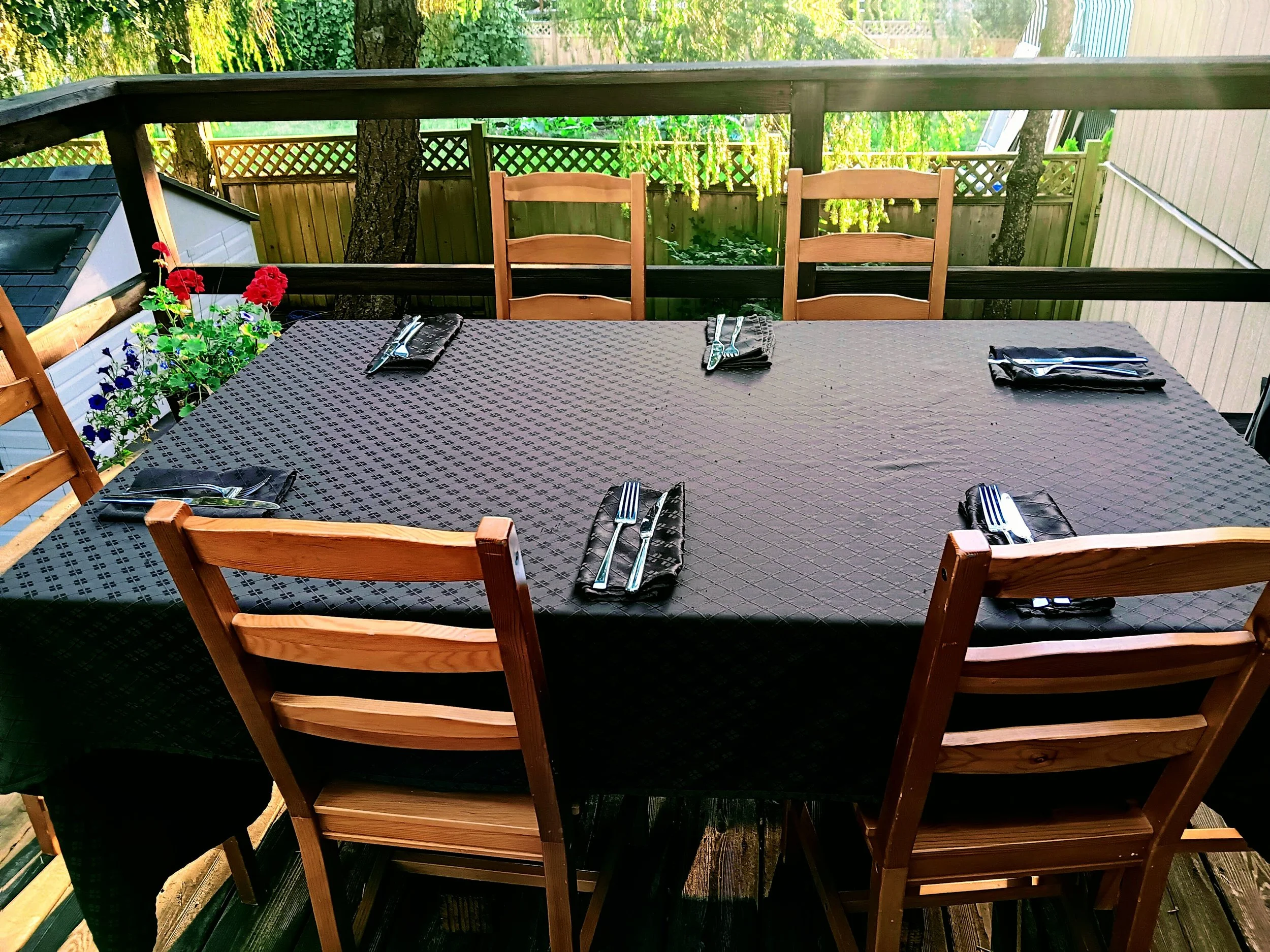 An outdoor dining table on the back patio with flowers in the summer
