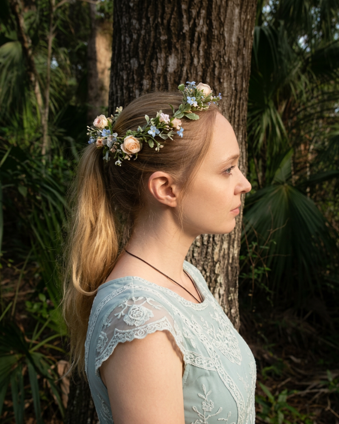 an enchanted fairytale woman in a ponytail with a lace blue dress and matching flower crown in the forest