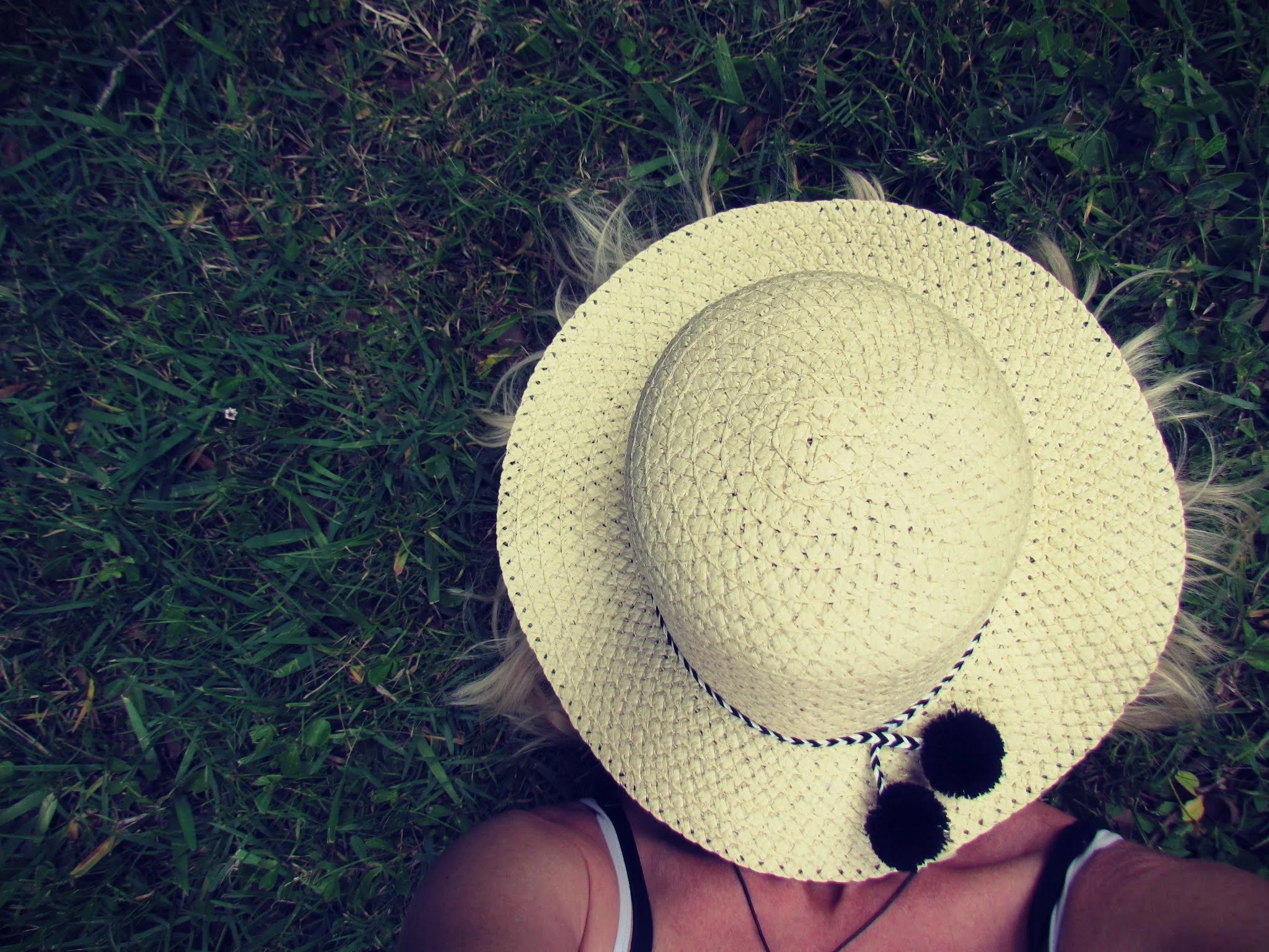 A woman lying in the dark green grass with a sun hat over her face