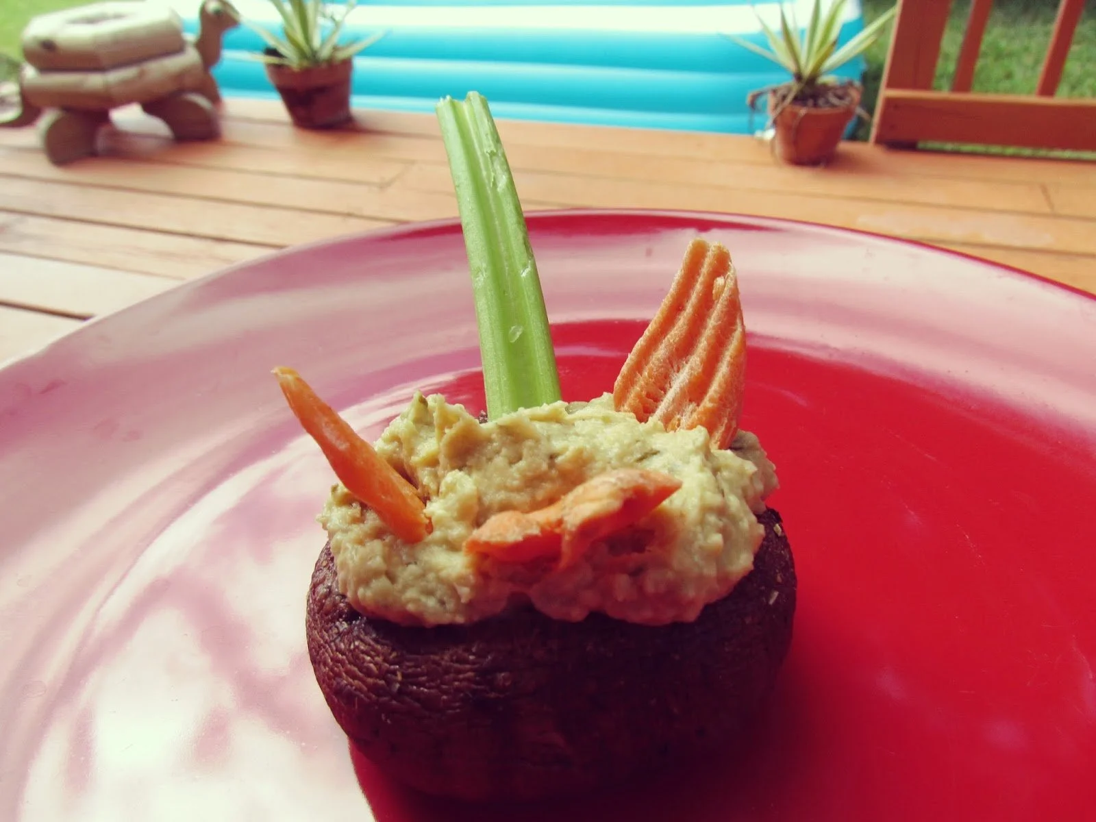 A mushroom cap filled with hummus and carrot and celery sticks