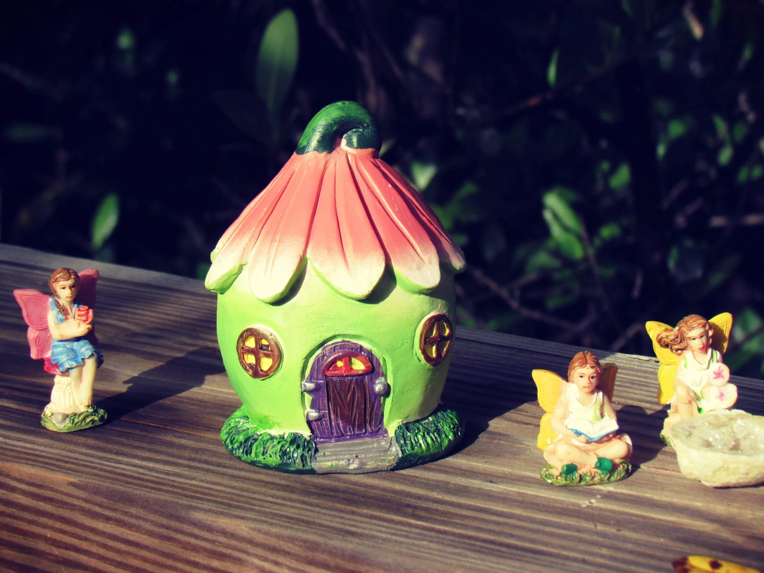 fairy house with pink petal roof surrounded by cute fairy figurines in the woods
