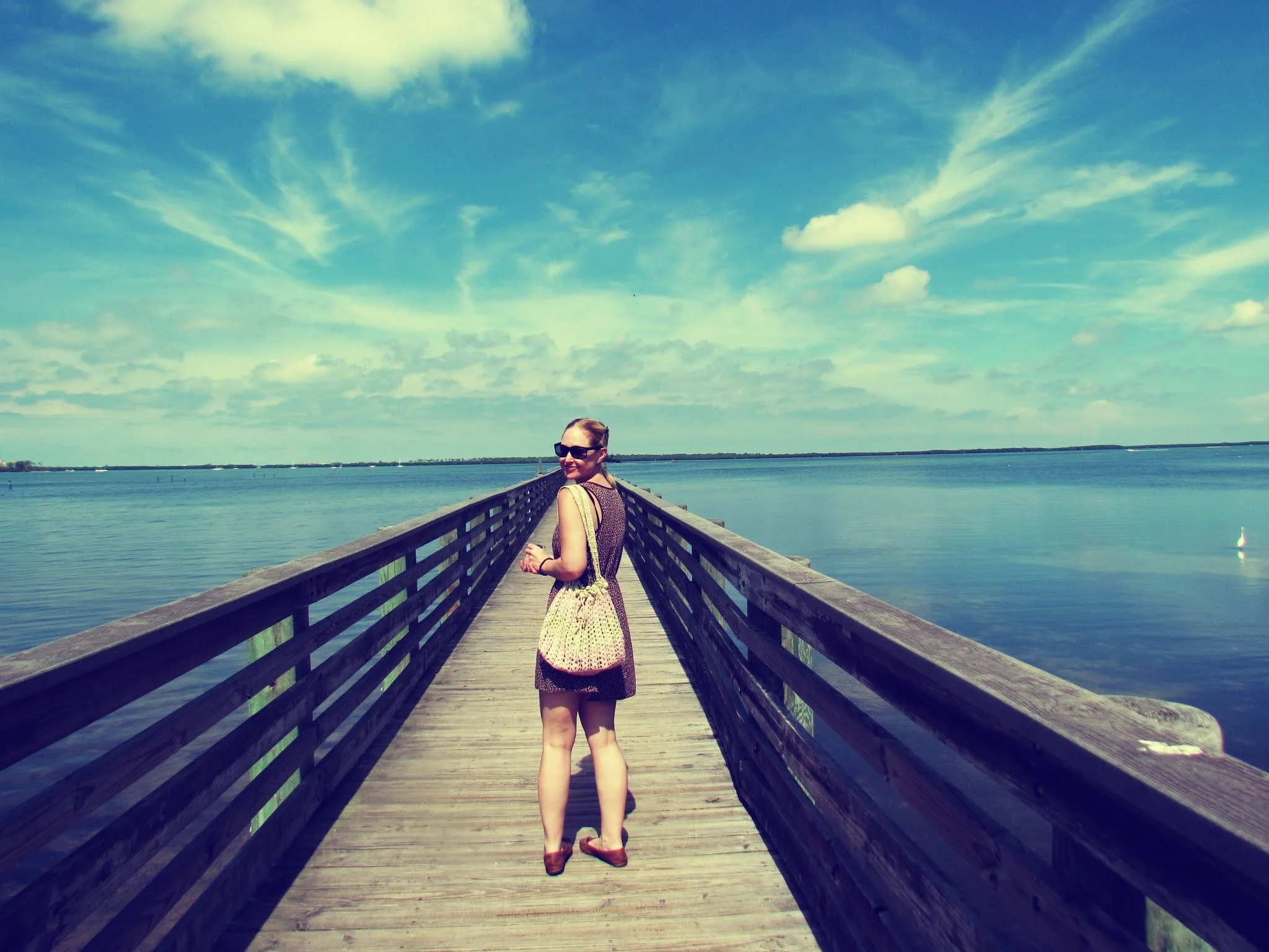 a woman in a tiny brown dress walking on the boardwalk at the pier surrounded by blue seas