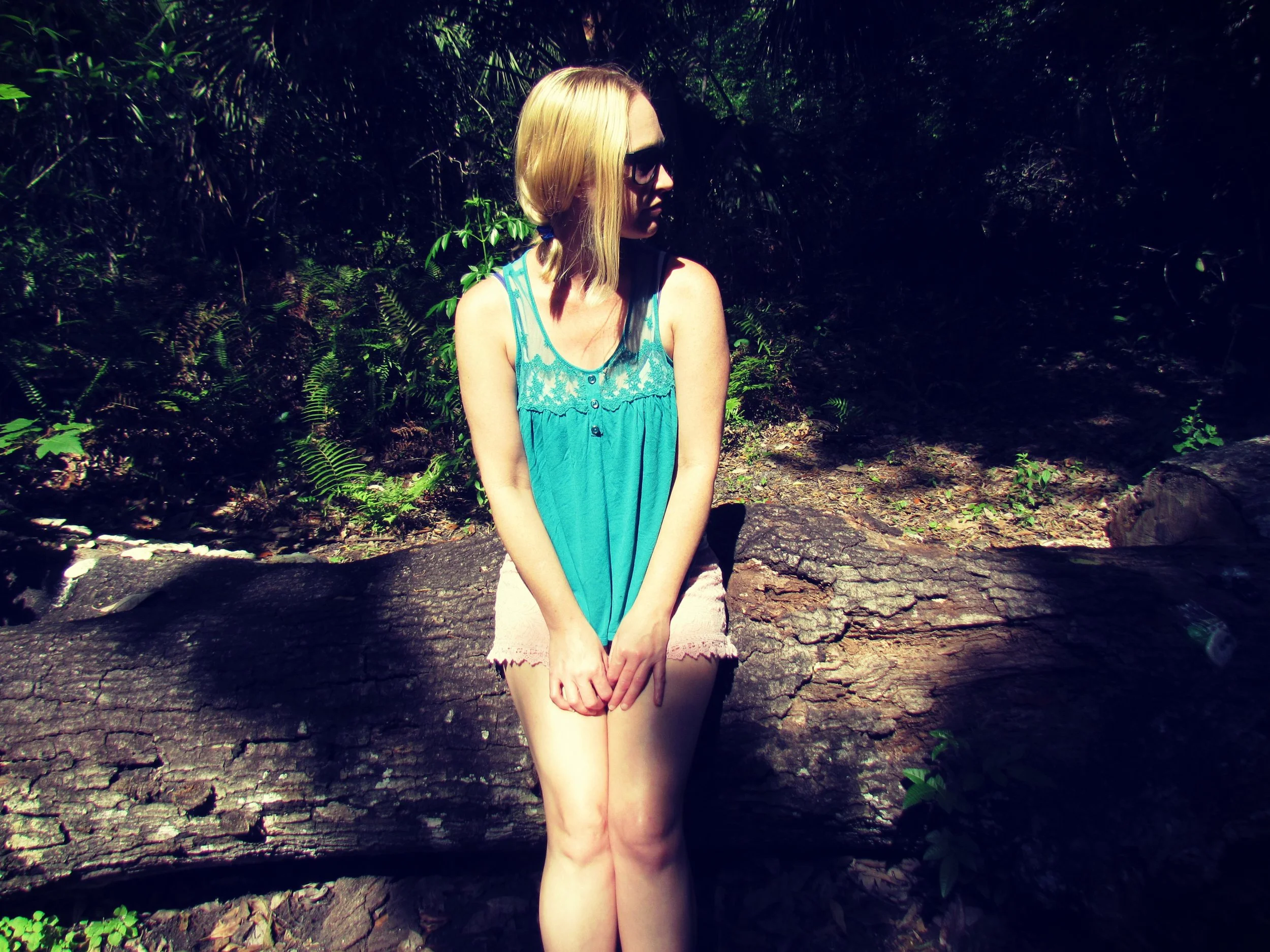 A blonde woman in pigtails sitting on a wooden logs in the forest on a hot summer's day