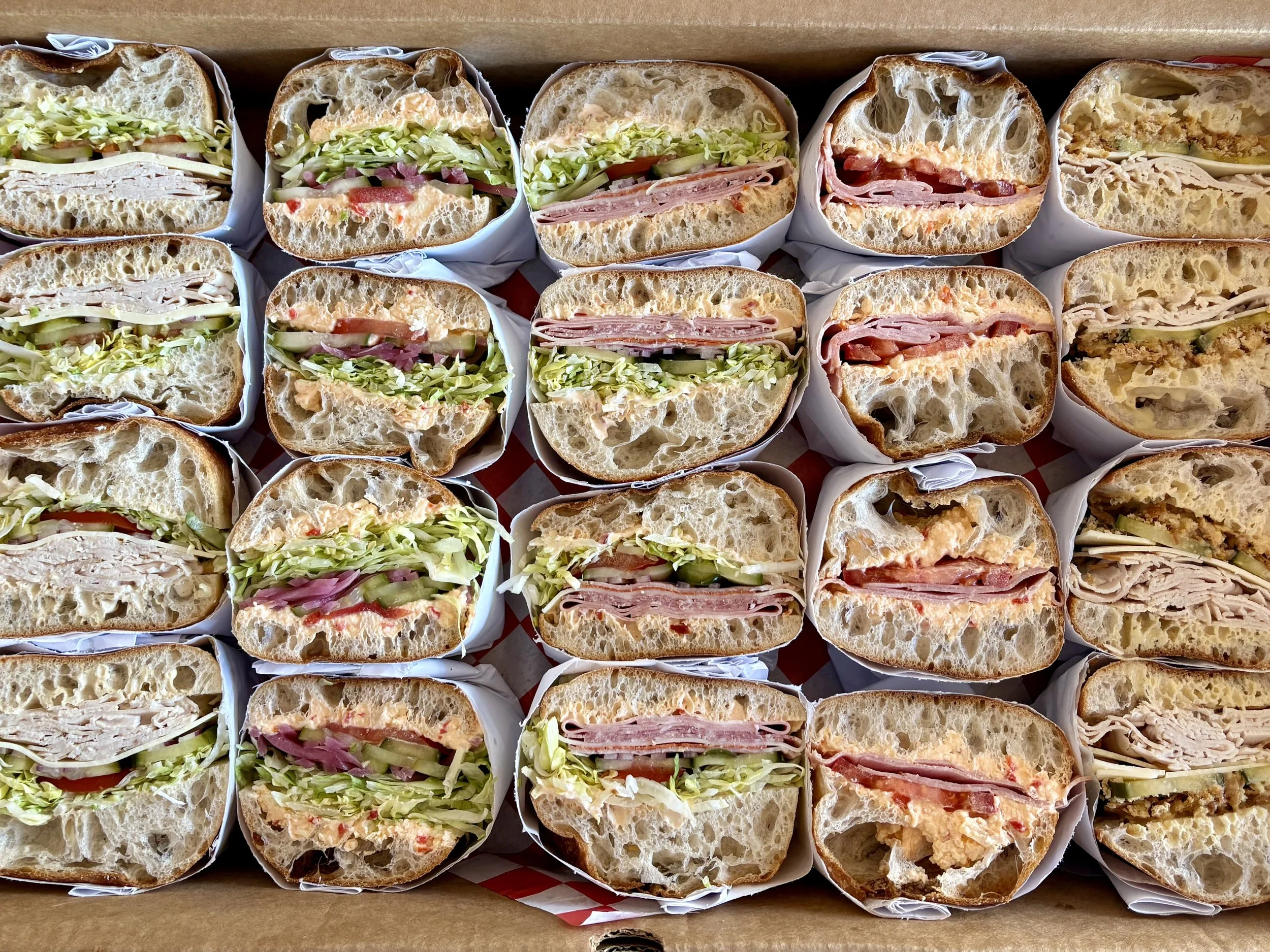 a tray of sandwiches, cut in half and face up so you can see the layers of bread, meats and vegetables.