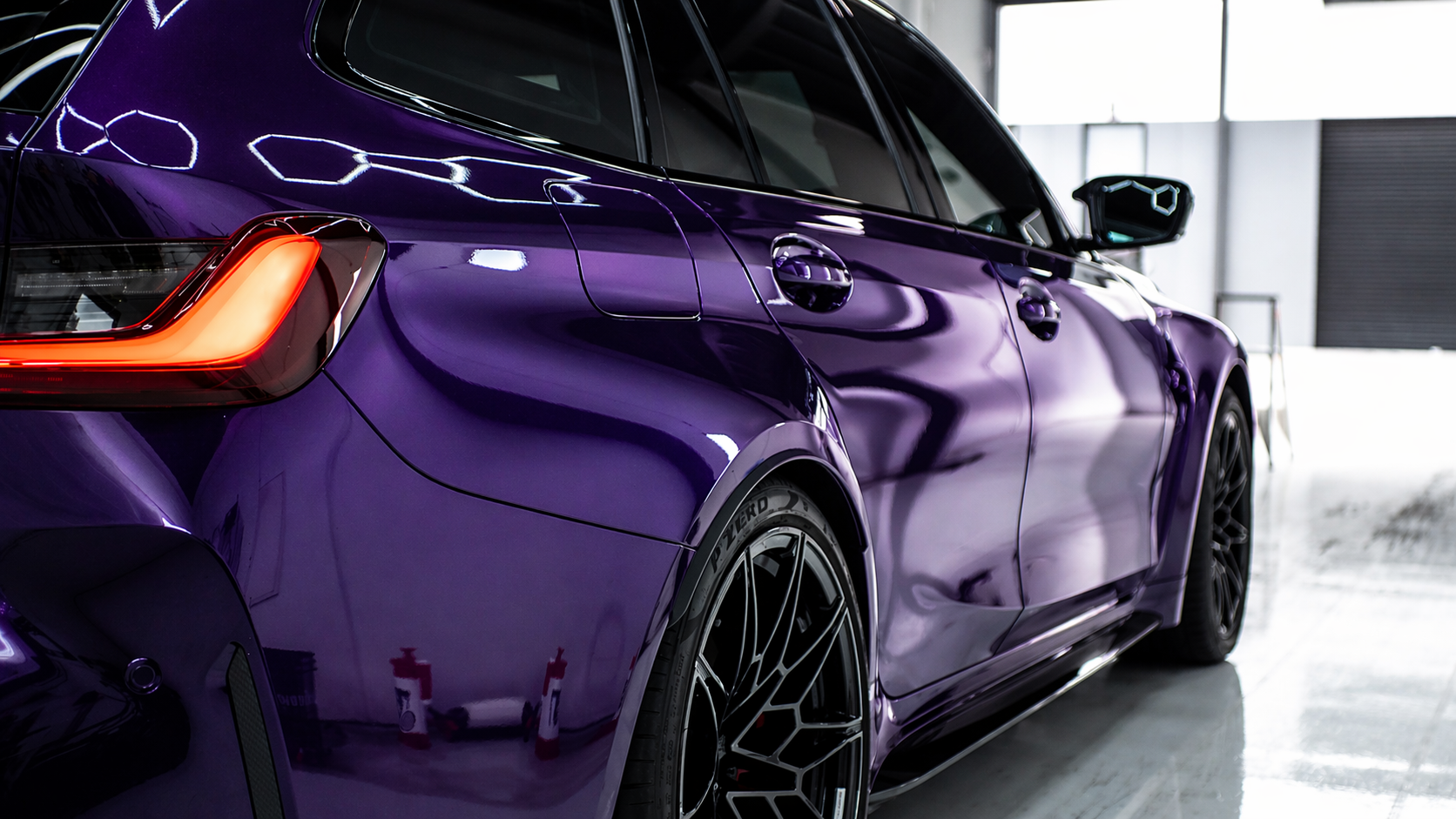 A purple sports car parked inside a building, showing the rear and side at an angle.
