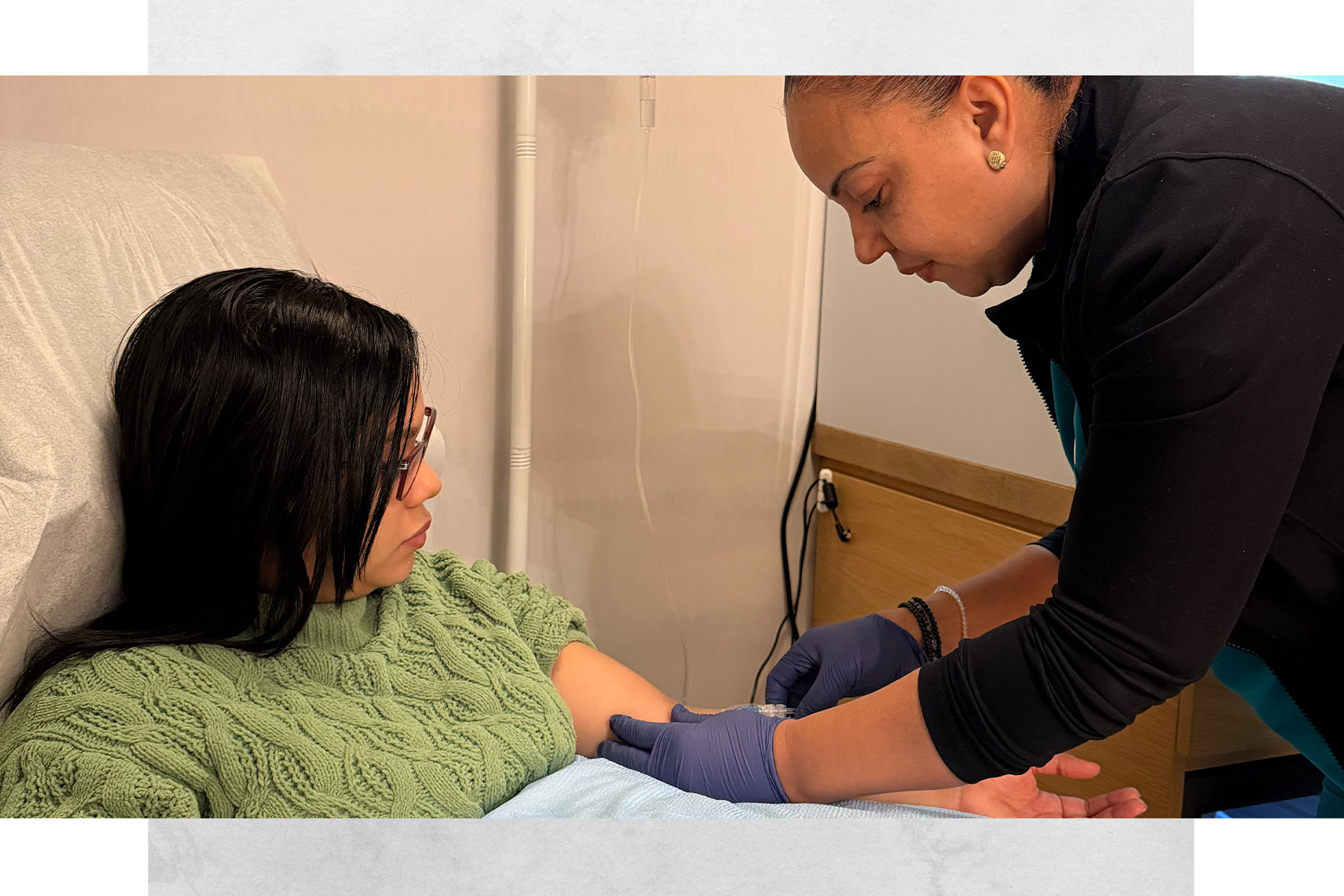 A healthcare professional wearing purple gloves is checking a patient's blood pressure in a hospital room.