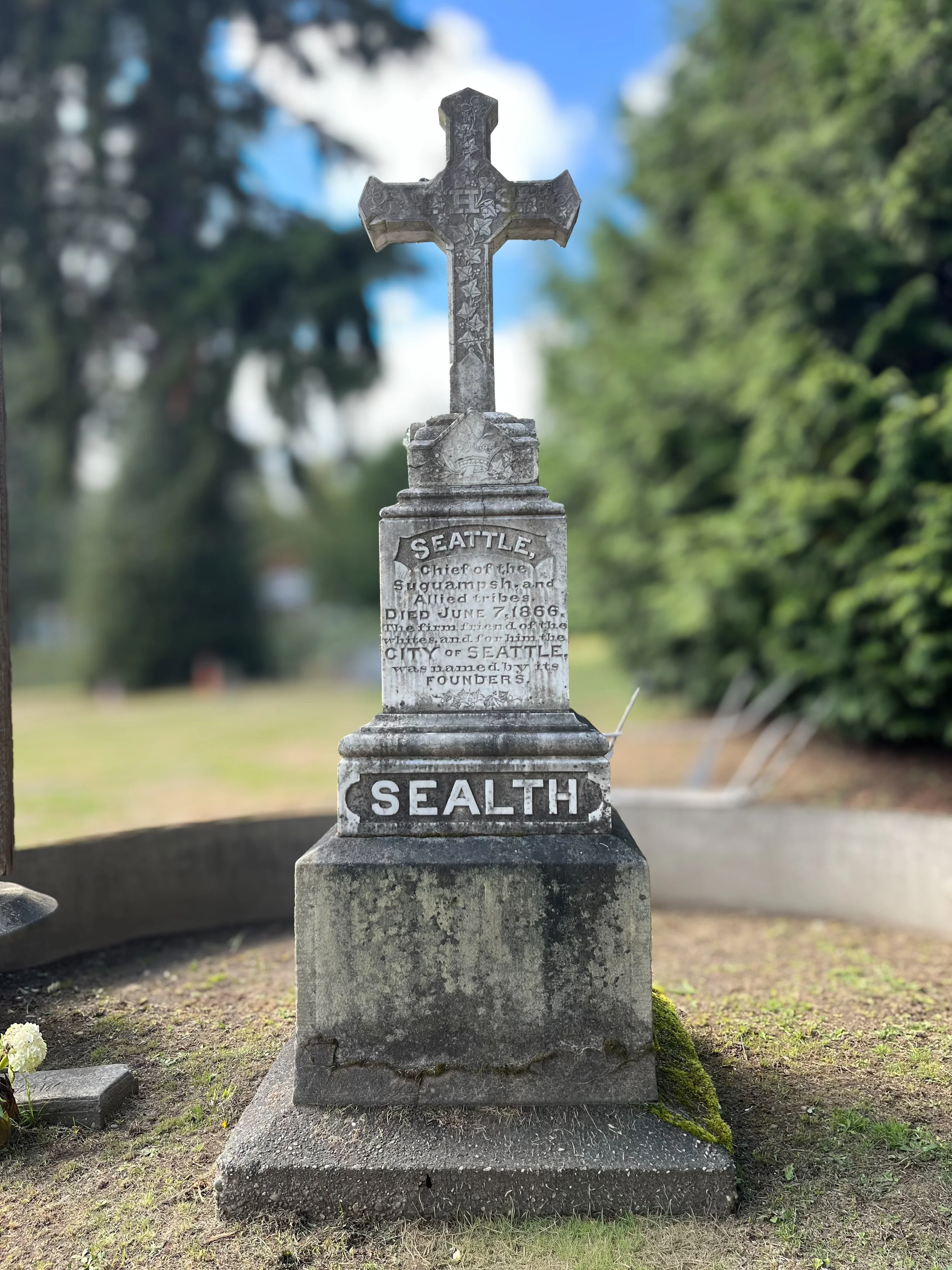 Gravestone with a cross at the top, inscribed with historical information about the founding of Seattle, Washington, by the Sealth family, who died in 1866.