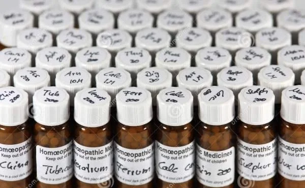 Multiple amber glass bottles of homeopathic medicine with white labels and handwritten names and dosages, arranged in rows.