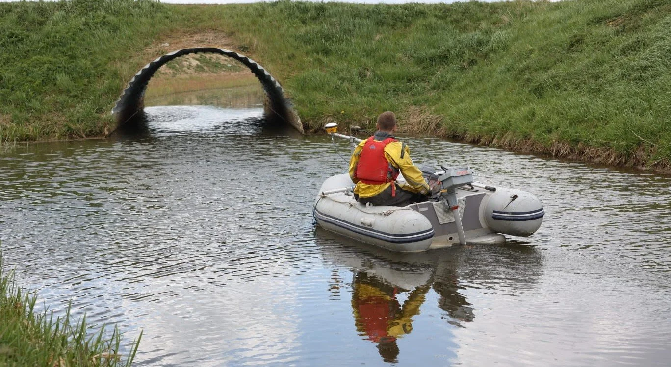 Image of a man conducting a bathymetry survey on a boat on a lake surrounded by coniferous forest 