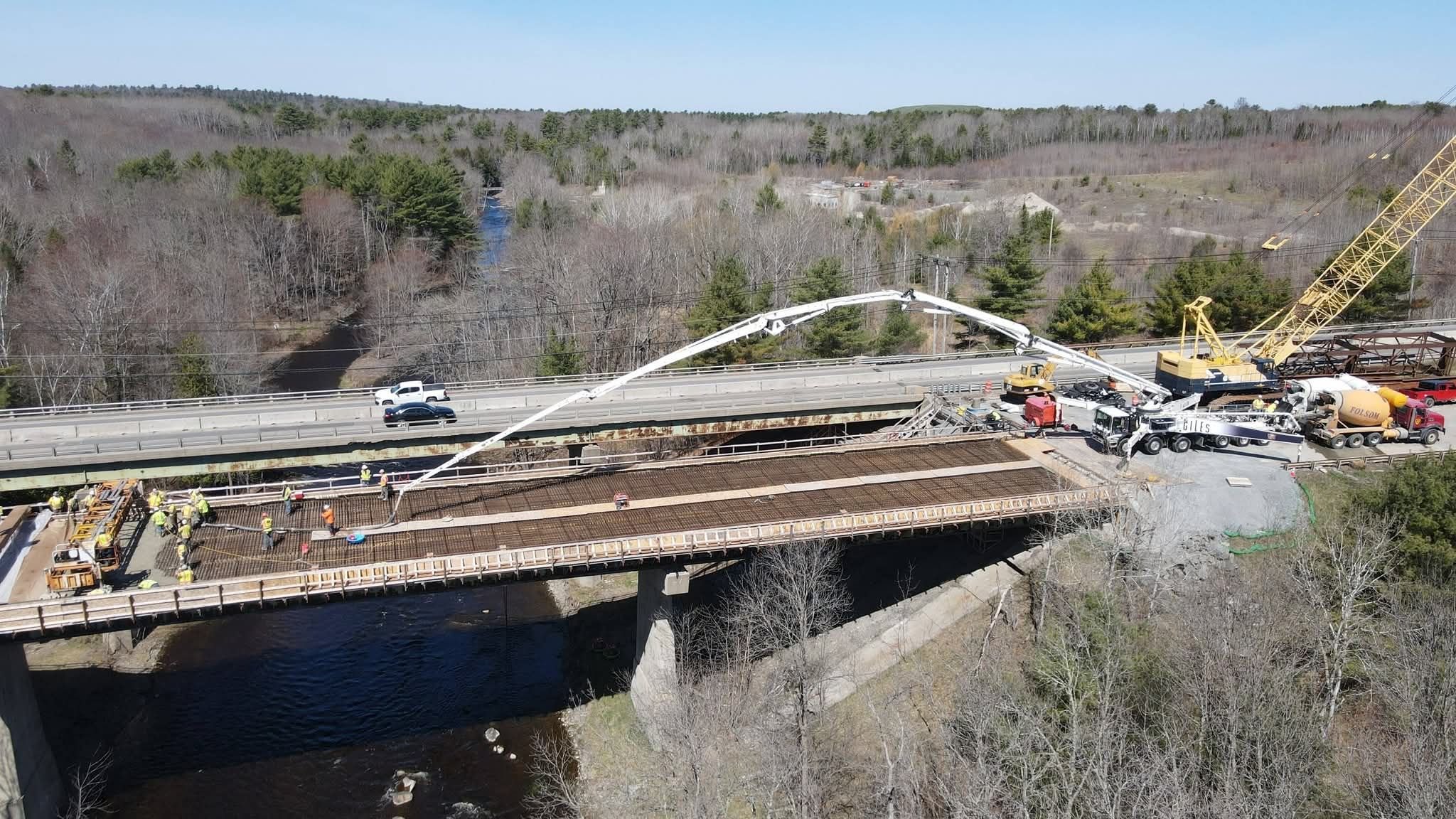 existing bridge with cars crossing with new bridge under constrction next to it with crew working and lots of concrete and crane equipment