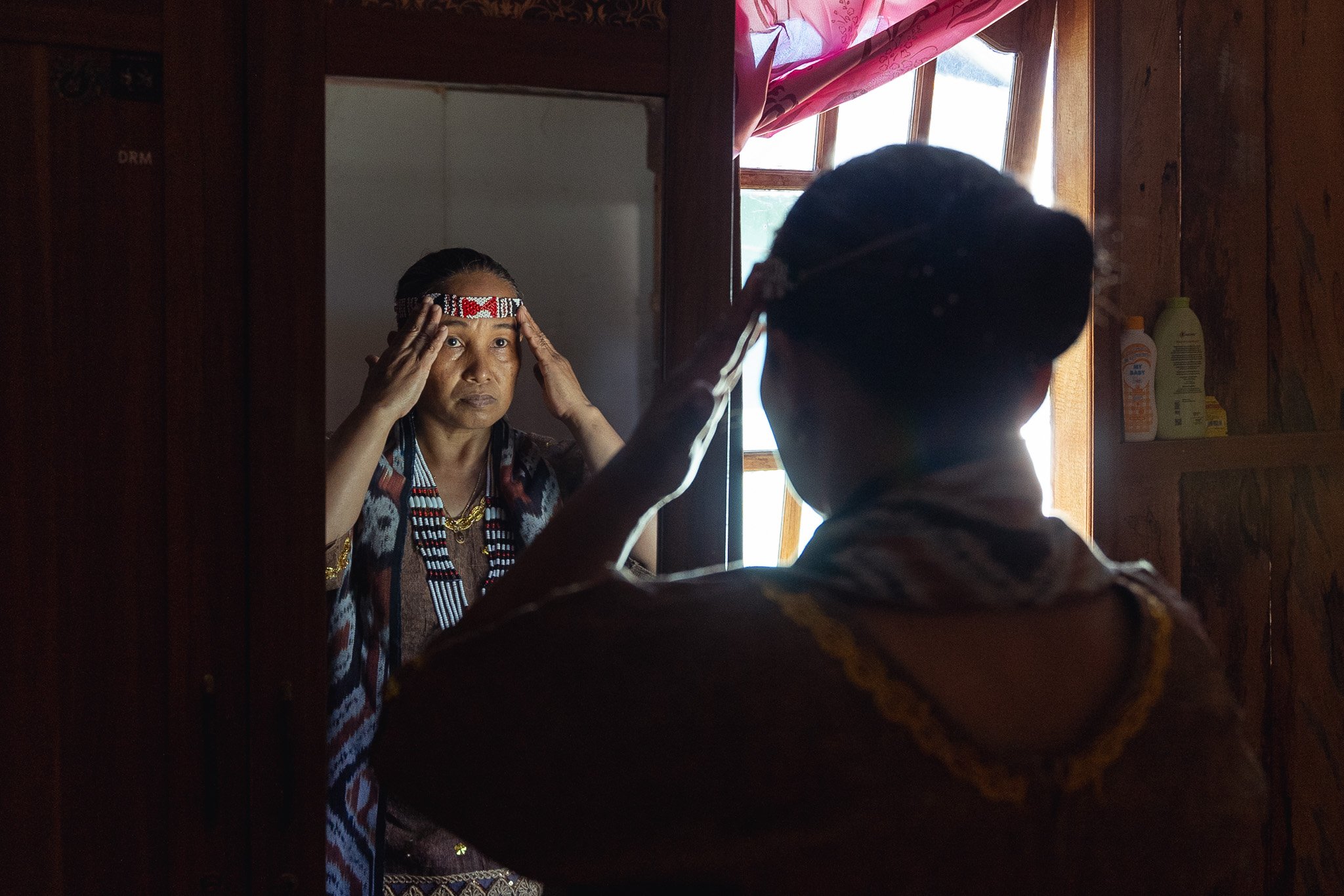 Rukmini Paata Toheke, an indigenous Kulawi leader or "Tina Ngata", fixes her decorative headband in a mirror, shot for UN Women (Central Sulawesi, Indonesia)