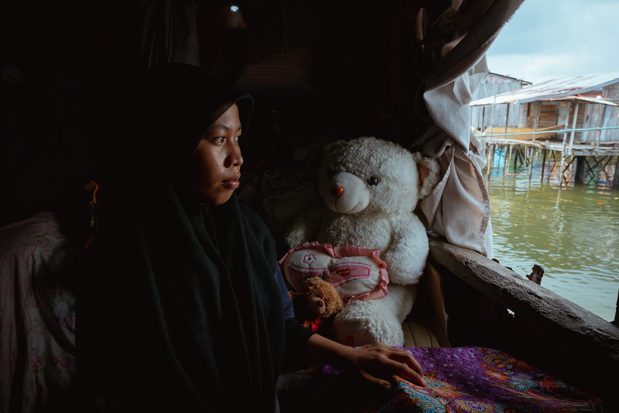 Suhaimah, a stateless teenager, gazes out of the window of her floating home, shot for UNDP. (Sabah, Malaysia)