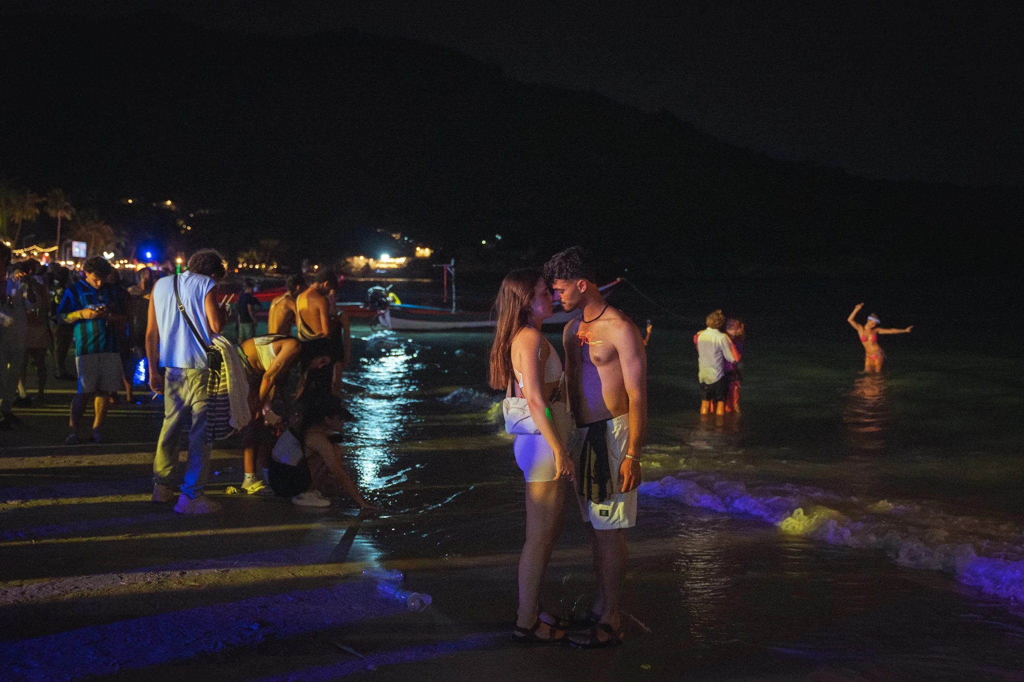 A couple share an intimate moment while revellers around then inspect the ocean water.