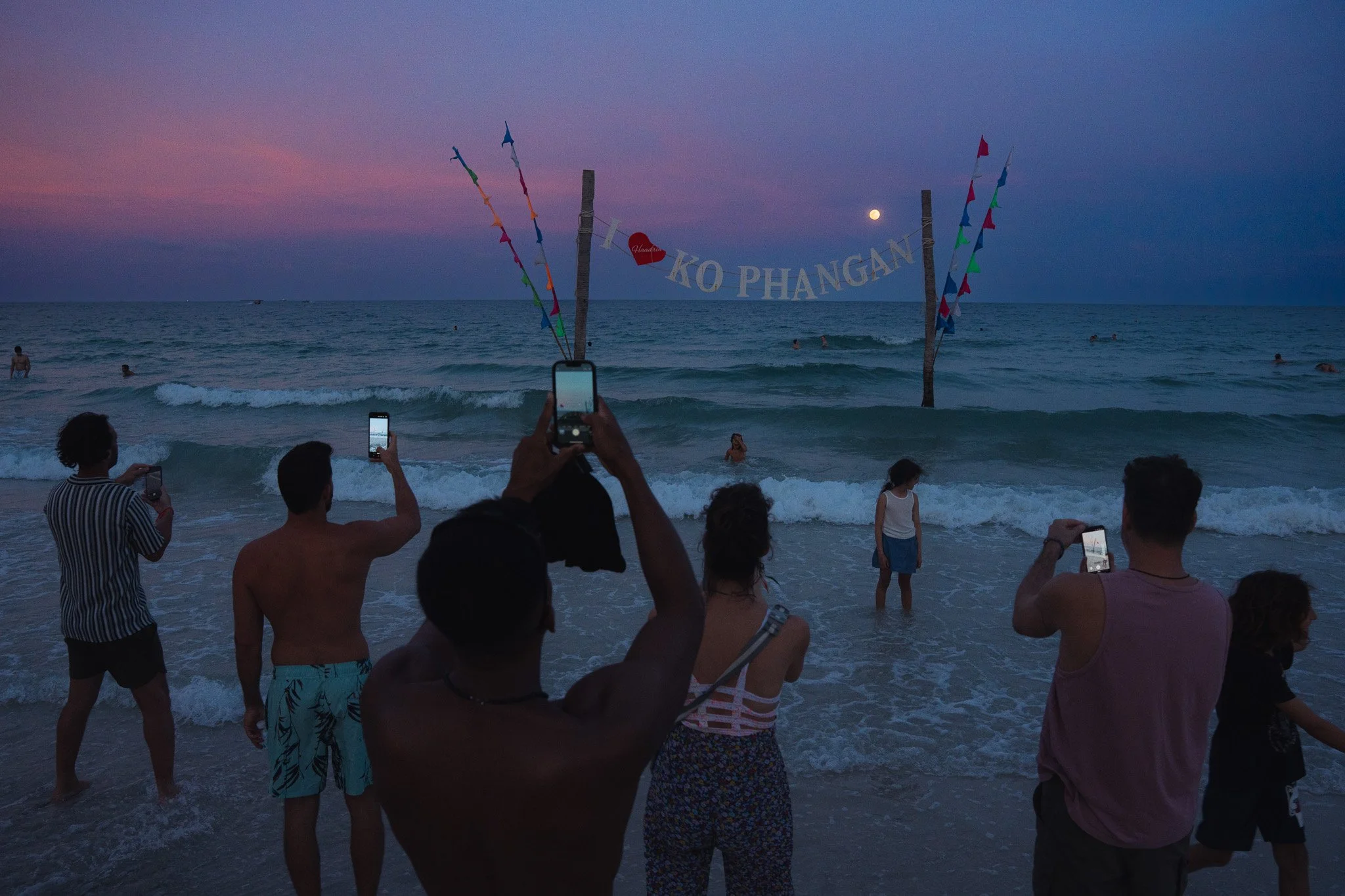 Tourists document the moonrise on their phones on Haan Rin beach, the site of the Full Moon Party.