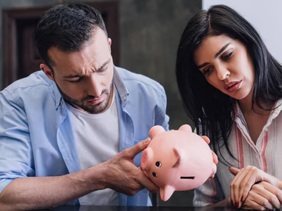 man and women stare forlorn and confused at a piggy bank they turn upside down, empty.