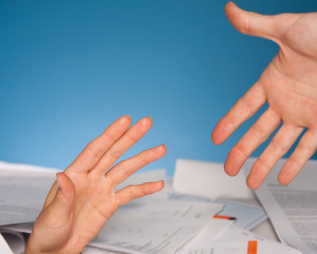 hand reaches out from a mountain of paperwork reaching out to a helping hand above