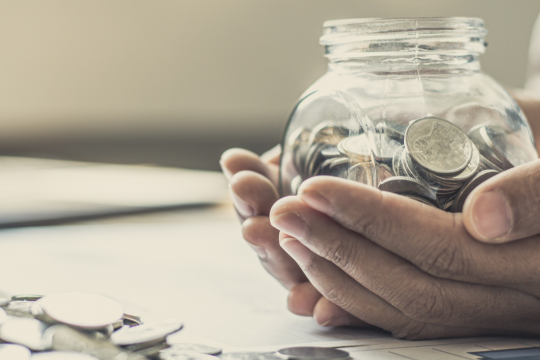 hands hold a jar of coins, coins scattered on the table nearby