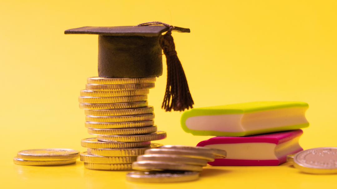 a tiny graduation cap and text books are atop a small stack of coins