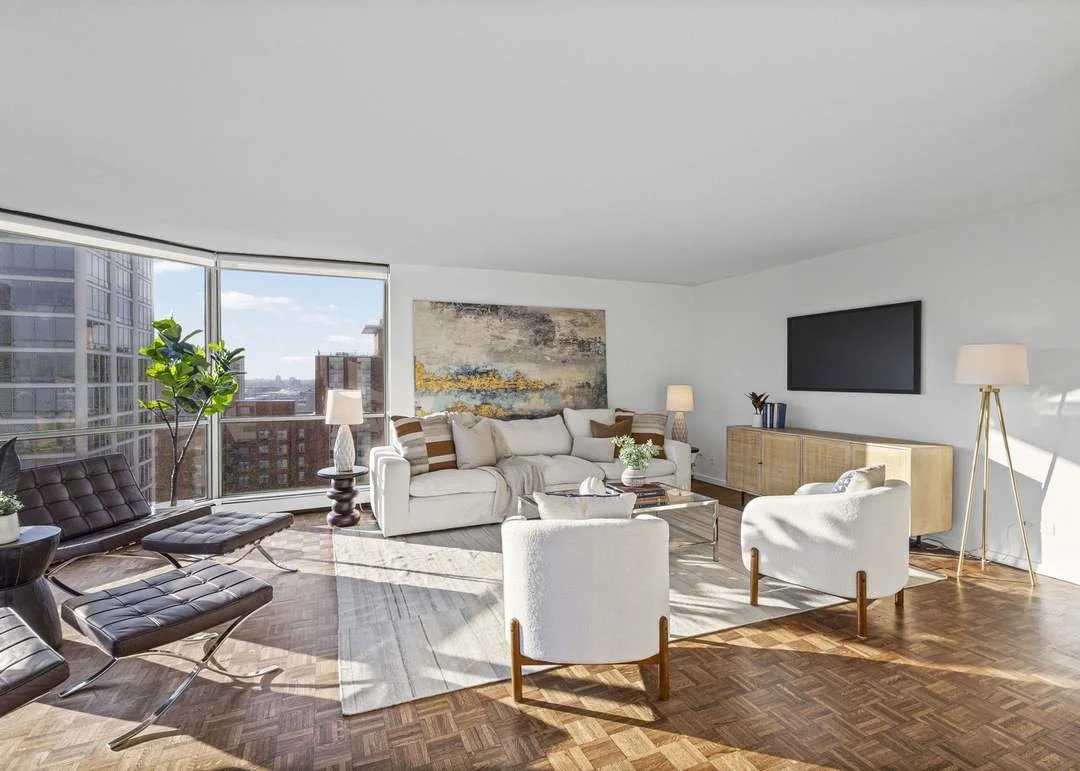 Modern living room with large windows, white sofa, black lounge chairs, and a flat-screen TV on the wall.
