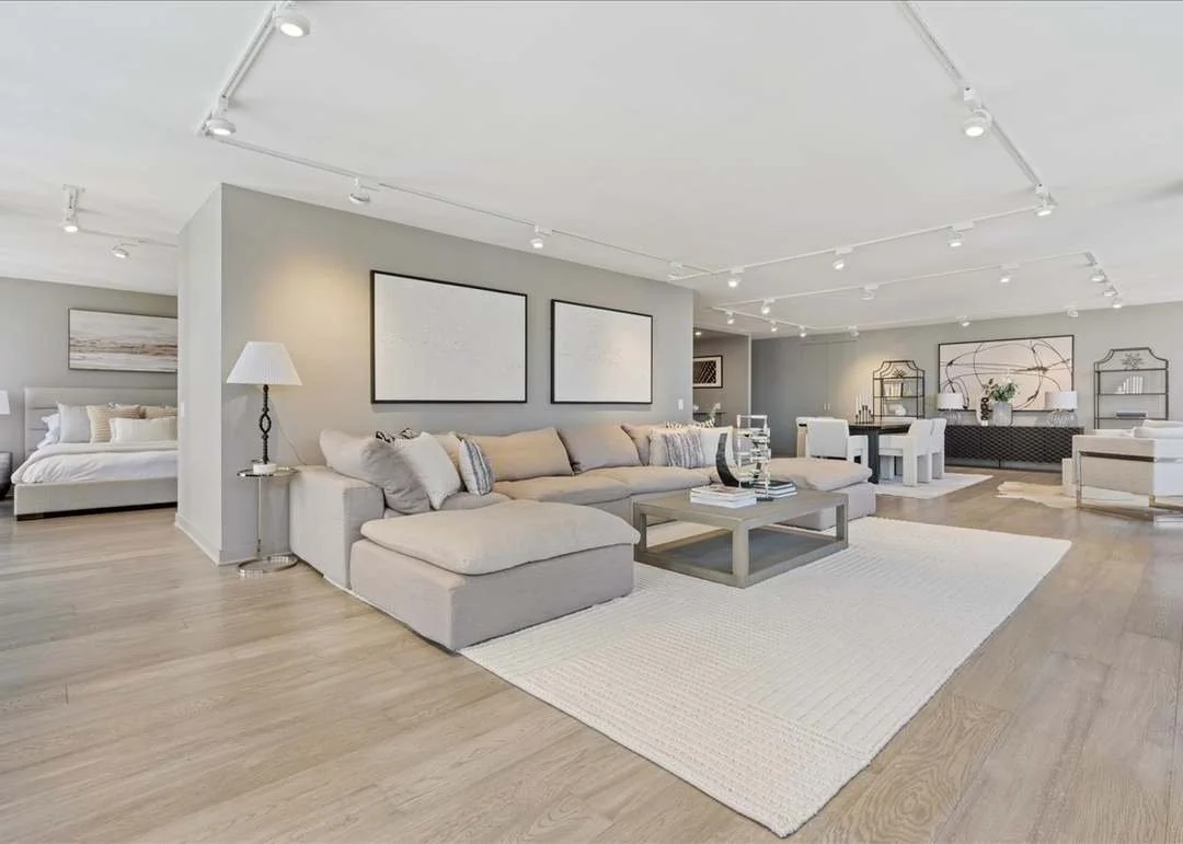 Modern open-concept living room with beige sectional sofa, white rug, light wood floors, and contemporary decor.