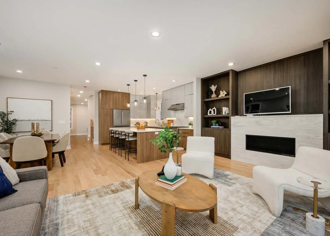 Open-concept living room and kitchen with wooden flooring, white walls, modern furniture, and built-in shelving.
