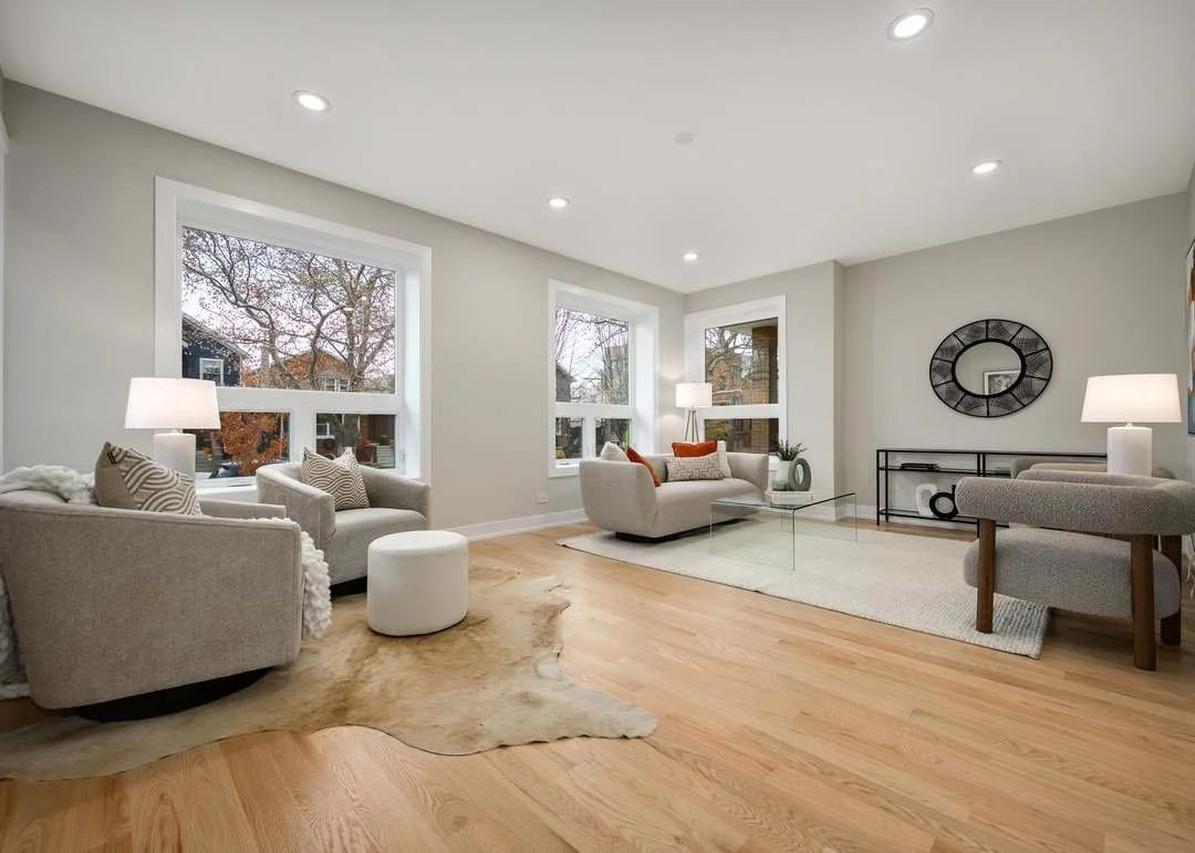 Bright living room with large windows, white sofas, area rug, wooden floor, and modern decor.