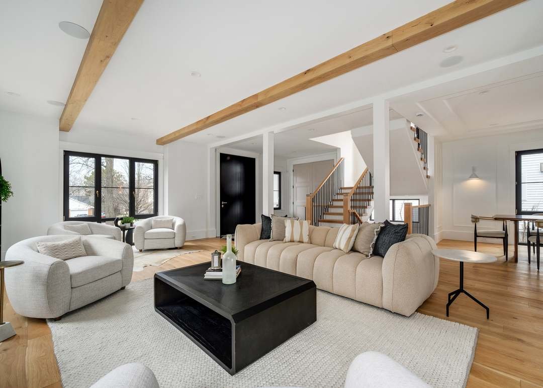 Living room with white couches, black coffee table, wood floors, large windows, staircase, and modern decor.