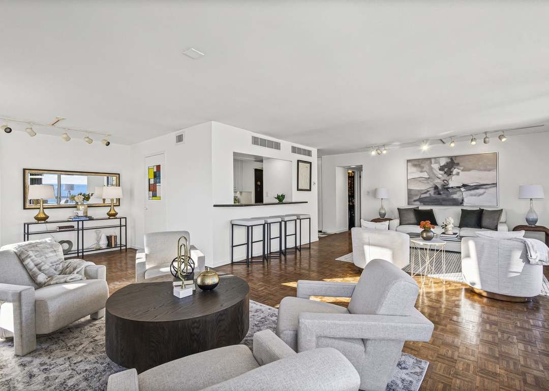 Spacious, modern living room with white walls, hardwood floors, multiple sofas, armchairs, and side tables, decorated with lamps, artwork, and decorative objects.