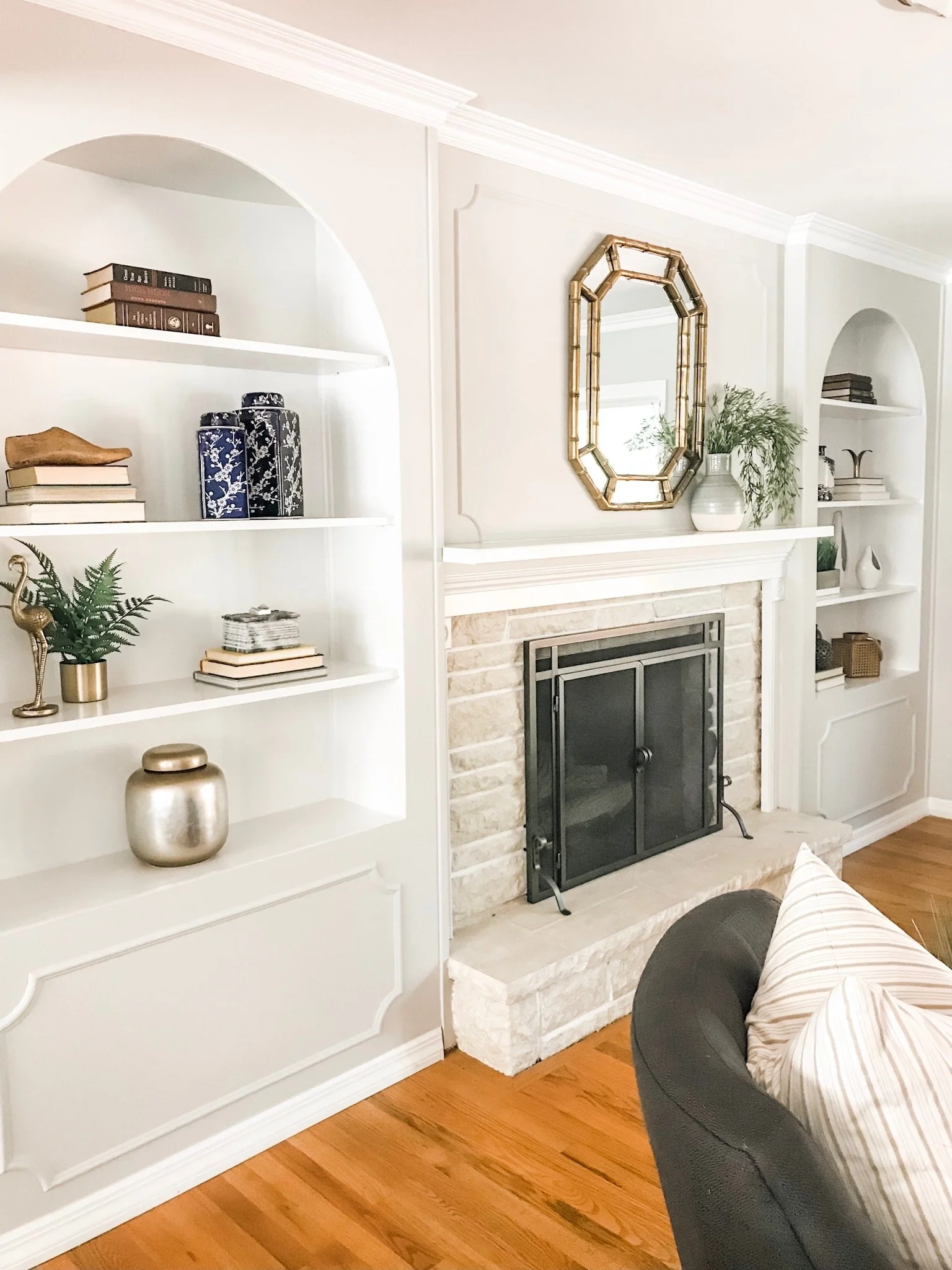 Living room with white built-in shelves, decorative items, and a stone fireplace with a brass framed mirror above. A completed luxury staging project in St. Louis.