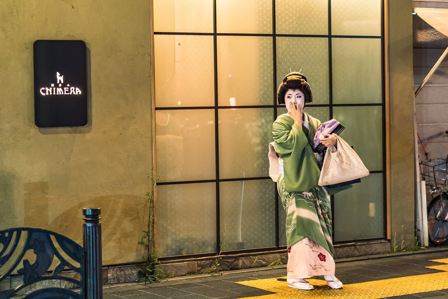 Una donna in kimono verde davanti alle vetrine di una strada giapponese, fotografata da Walter Stolfi.