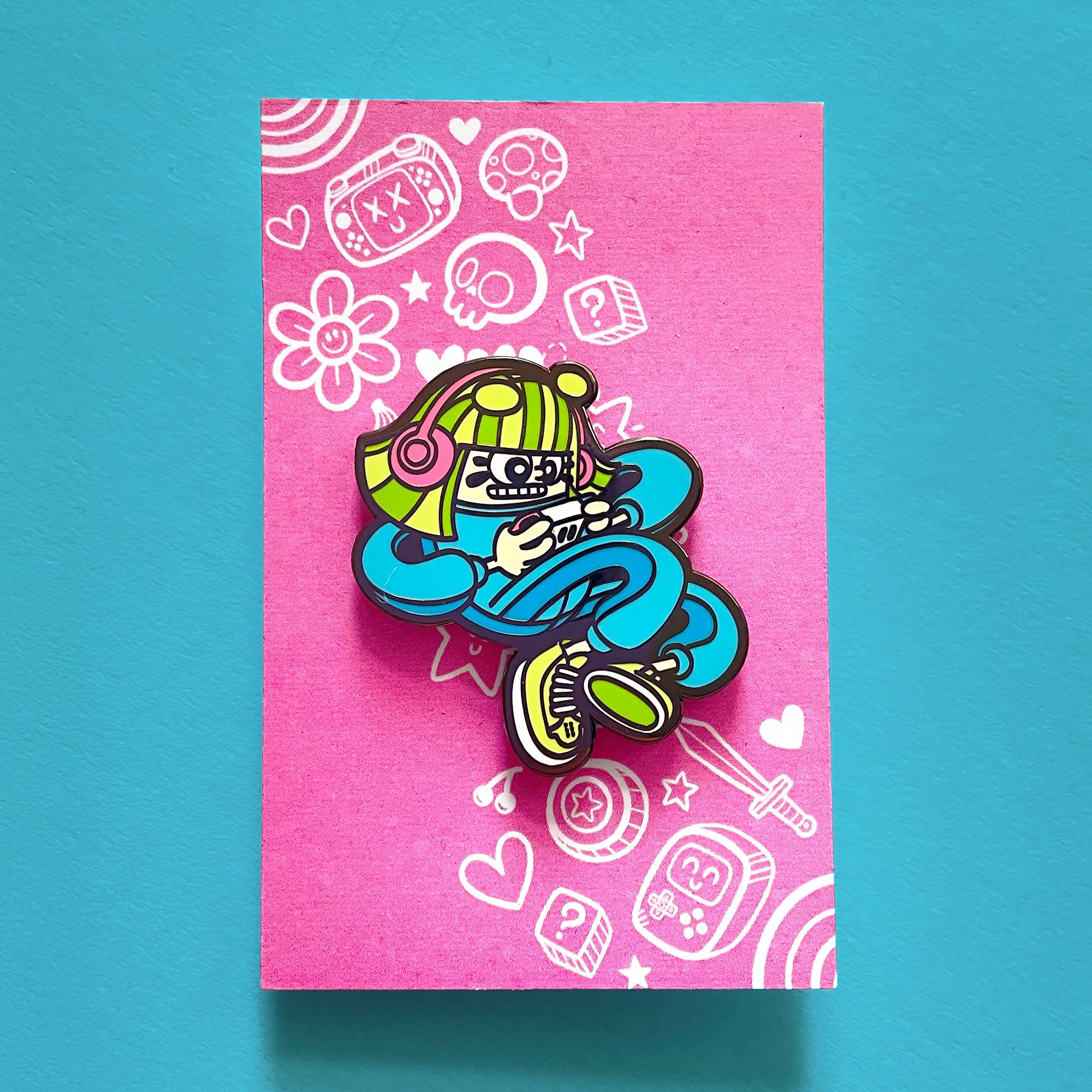 A photo of this Gamer Girl enamel pin on a pink backing card.