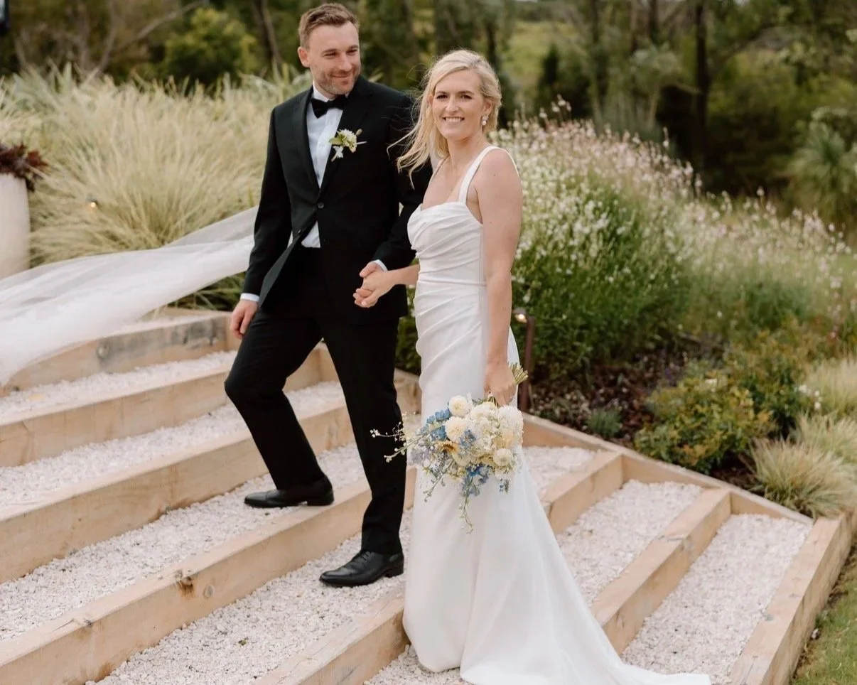 Bride and groom walking up white steps surrounded by greenery at an Auckland garden wedding.