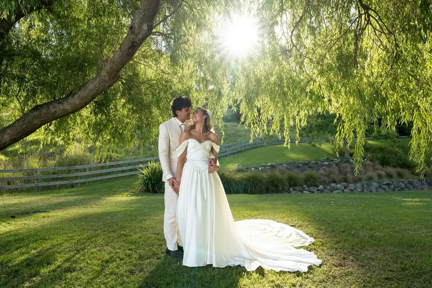 Newly married couple embracing under a willow tree as the sun goes down behind them